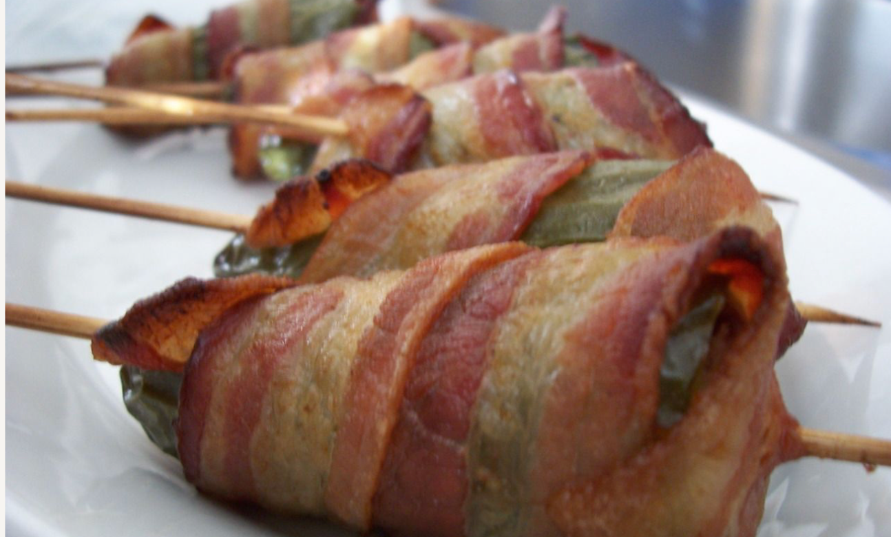 Bacon-wrapped jalapeño poppers on skewers arranged in a row on a white plate.