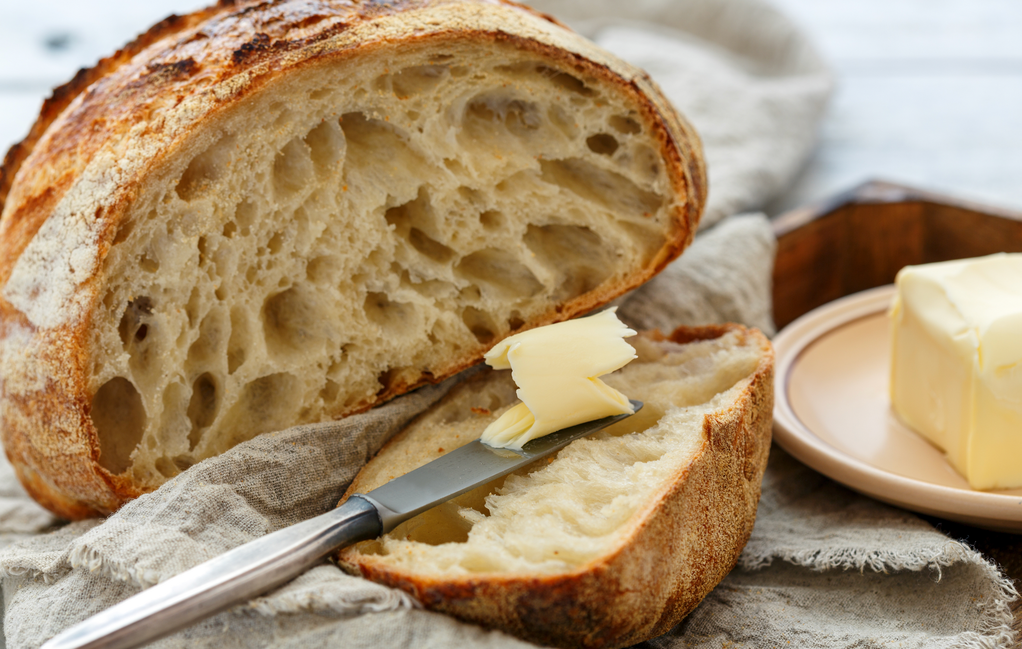 A loaf of crusty bread with a slice spread with butter, a knife, and a block of butter on a plate.