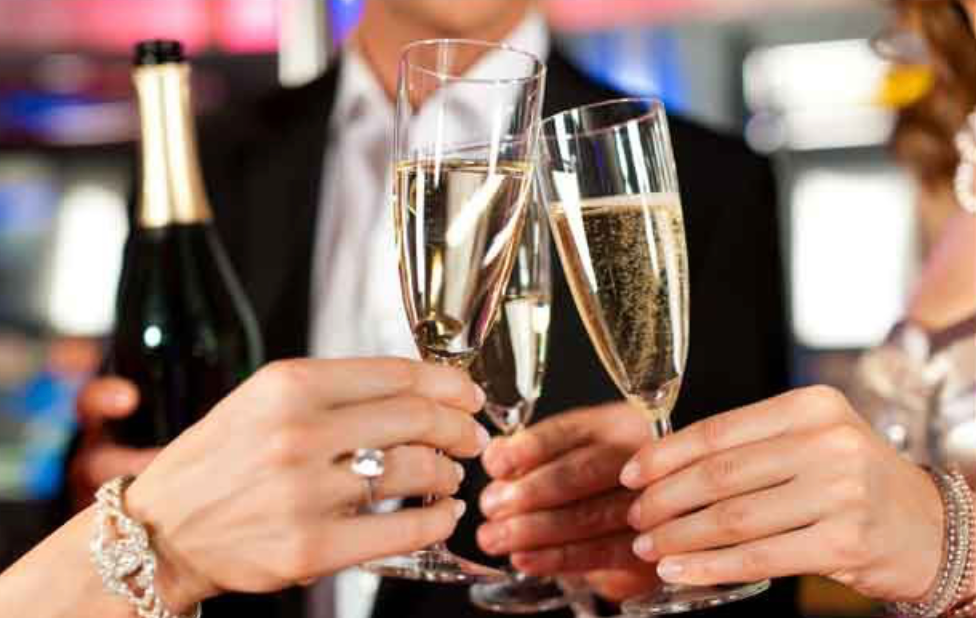 People clinking filled champagne flutes together, with one person holding a bottle in the background.