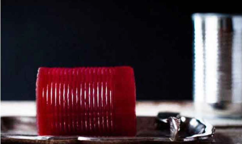Cylindrical slab of canned cranberry sauce standing upright beside an opened tin can.