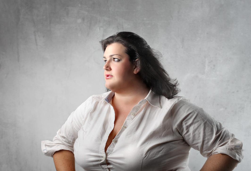 A woman in a white shirt looks to the side with her hands on her hips against a gray textured background.