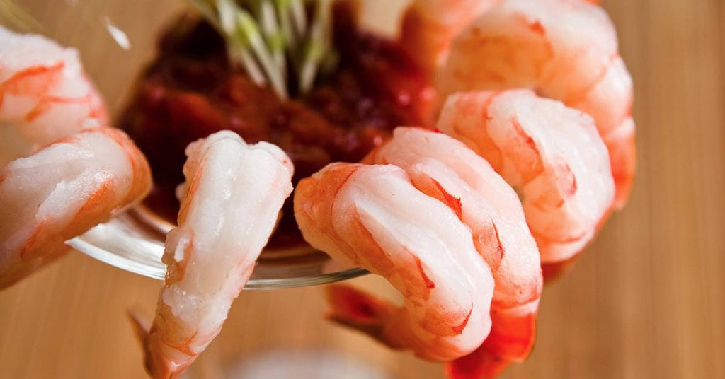 Chilled shrimp arranged on a glass rim with cocktail sauce in the center.