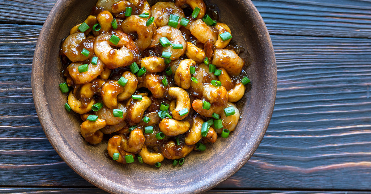 Bowl of glazed cashew chicken topped with chopped green onions on a dark wooden table.