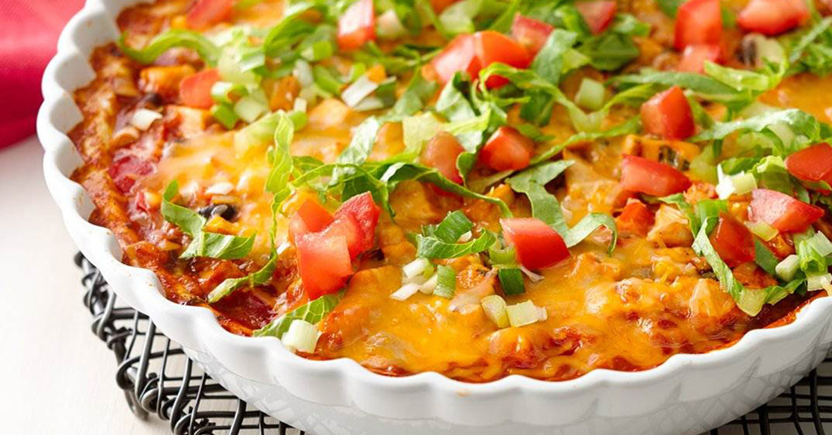 Cheesy baked dish topped with lettuce, diced tomatoes, and green onions in a white pie dish.