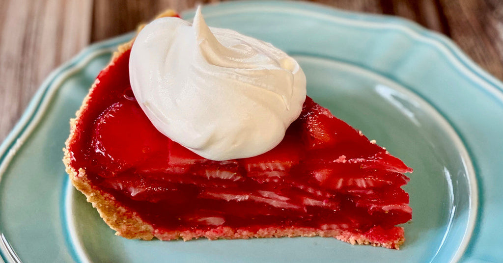 Slice of strawberry pie with glossy filling and a dollop of whipped cream on a light blue plate.