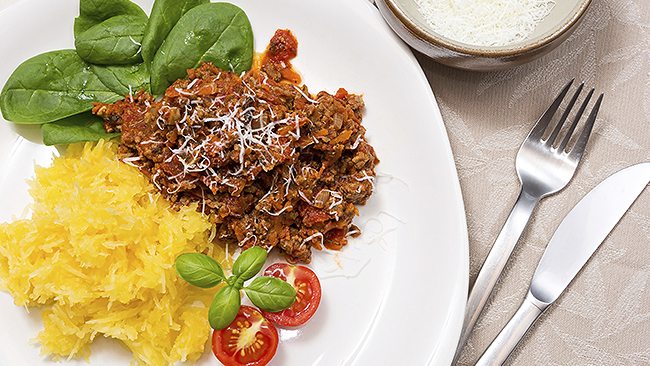 Plate with shredded squash, spinach, tomato garnish, and a saucy meat dish topped with grated cheese.