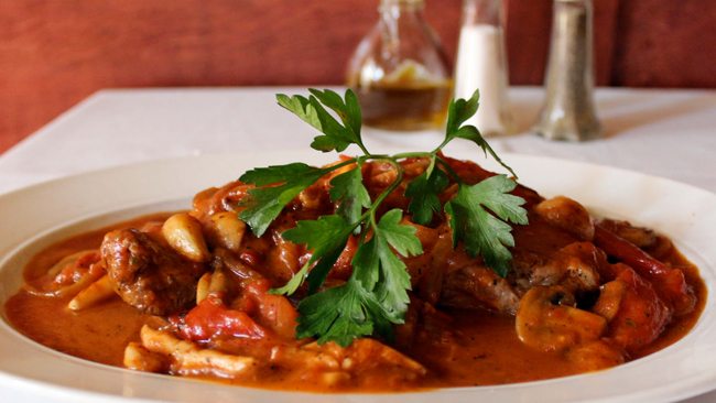 Plate of chicken in a rich tomato sauce with mushrooms and peppers, topped with fresh parsley.
