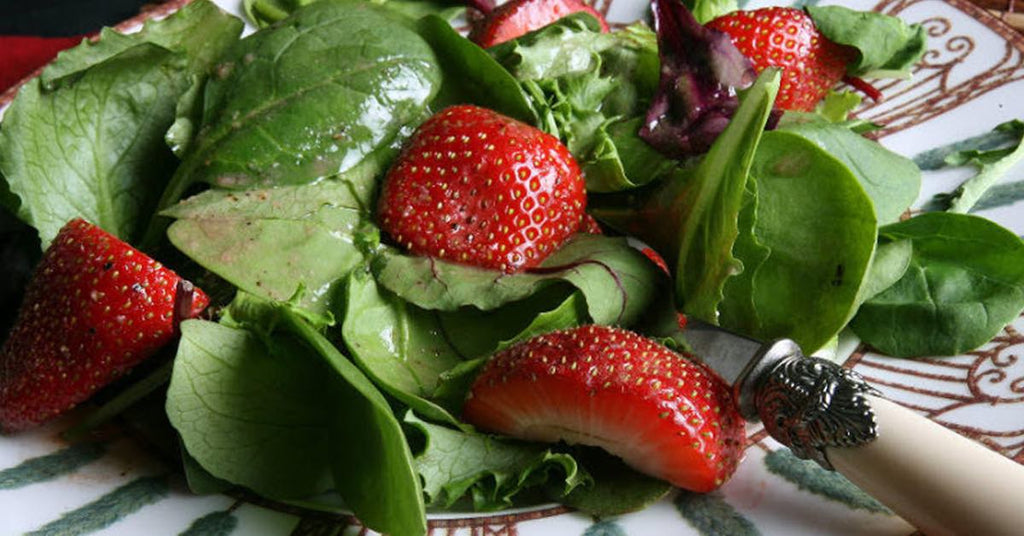 Fresh spinach and mixed greens salad topped with sliced strawberries on a decorative plate.