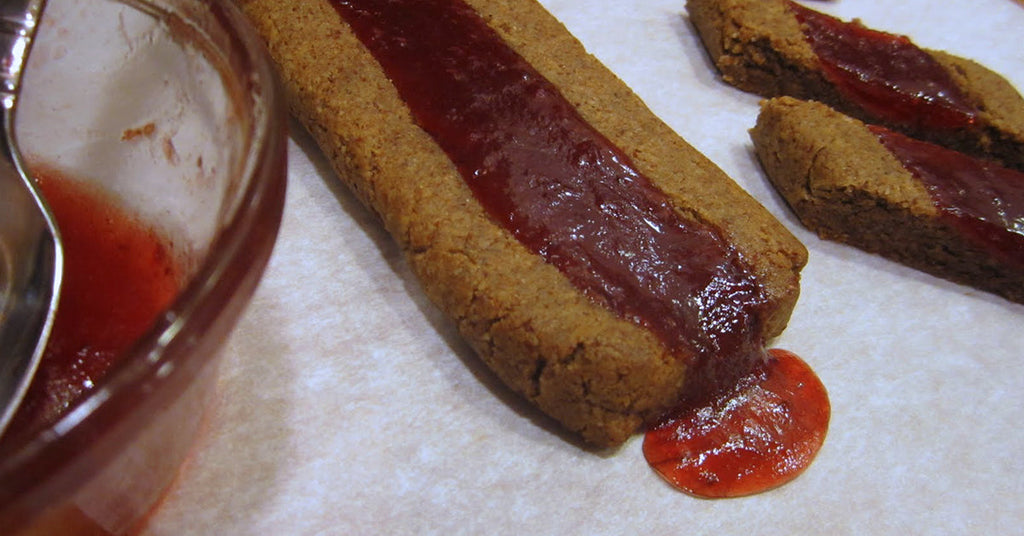 Baked cookie bars with a strip of red fruit filling oozing onto the parchment paper.