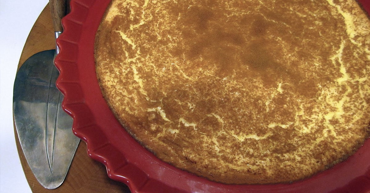 Golden-brown baked custard pie in a red dish with a metal pie server beside it.