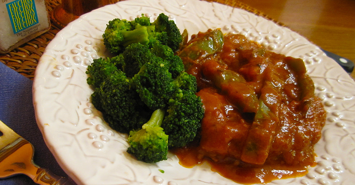 Steamed broccoli served beside a plate of vegetables in a thick red tomato based sauce.