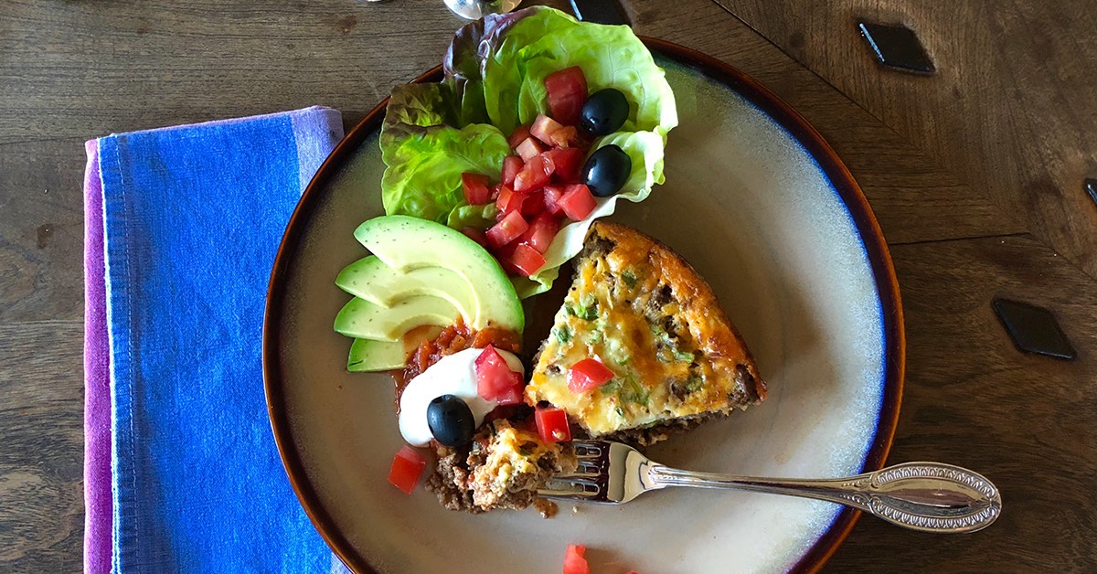 Plate with a slice of savory casserole, avocado, lettuce with tomatoes and olives, plus sour cream and salsa on the side.