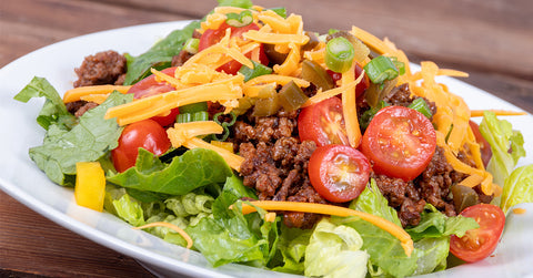 Taco salad with seasoned beef, lettuce, cherry tomatoes, cheddar cheese, and green onions.