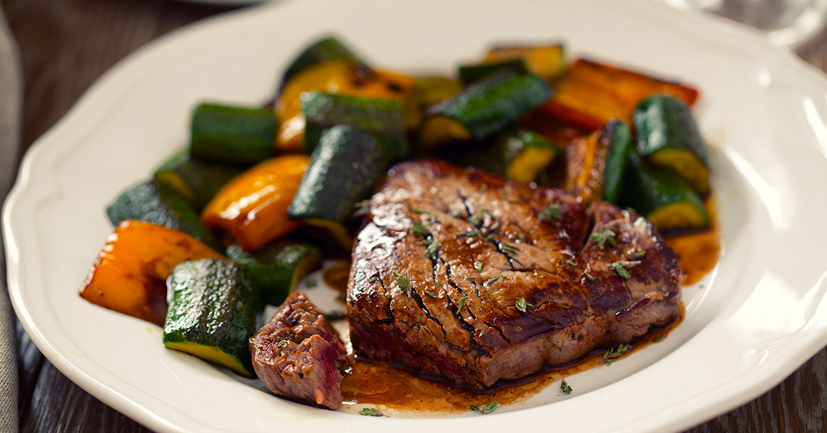 Grilled steak served with roasted zucchini and bell peppers on a white plate.
