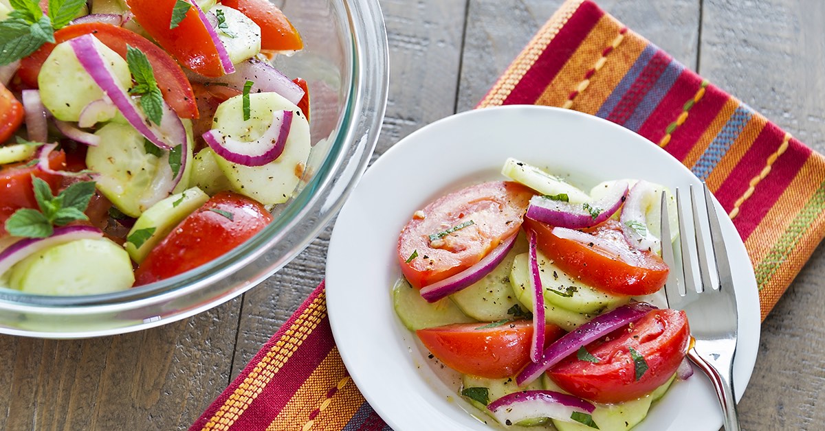 Cucumber, tomato, and red onion salad with herbs served in a bowl and on a white plate.