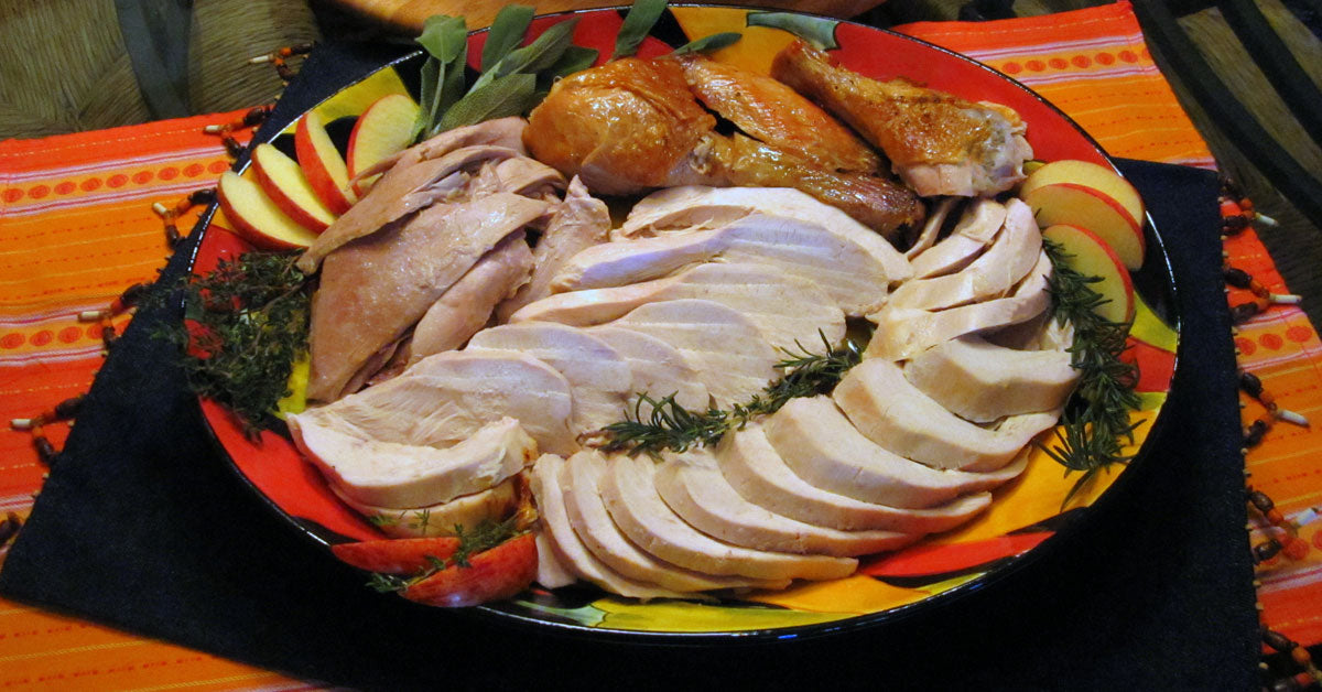 Platter of sliced roasted turkey with herbs and apple slices arranged on a colorful serving dish.