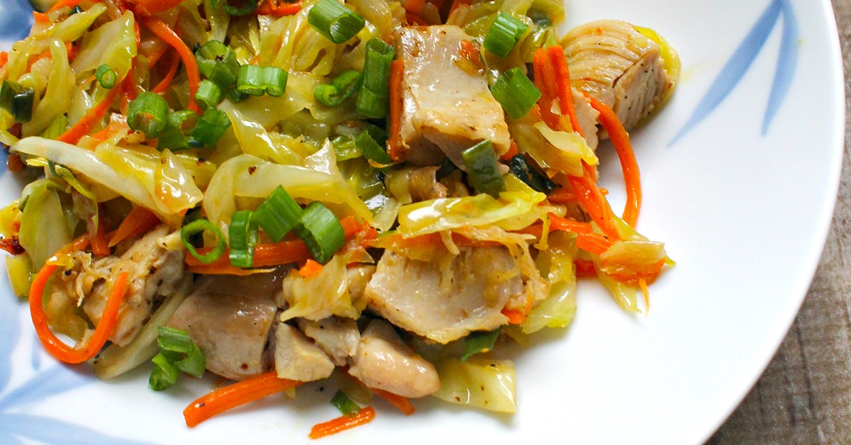 Stir-fried chicken with cabbage, carrots, and green onions served on a white plate.
