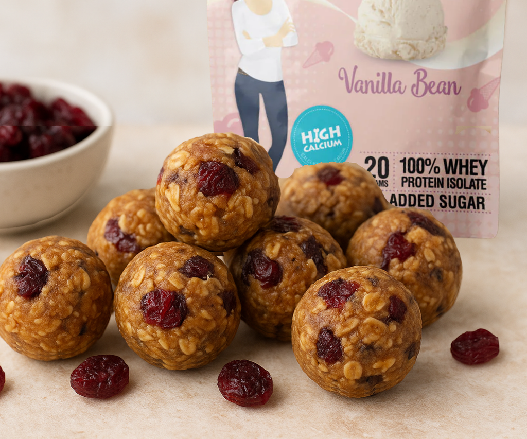 Oat and cranberry protein balls arranged on a surface with dried cranberries and a vanilla protein powder bag behind them.