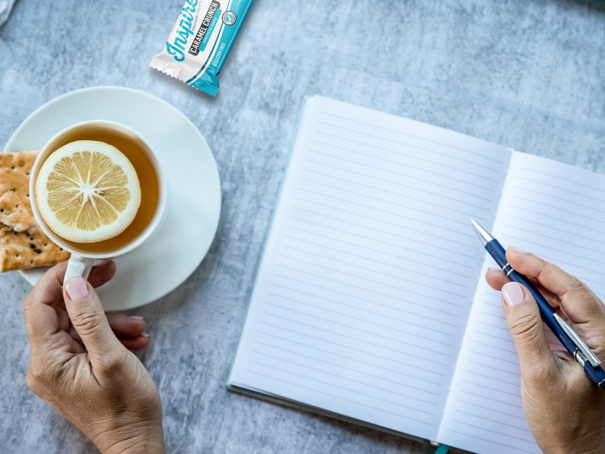 Hands journaling with a warm cup of tea reflecting on goals
