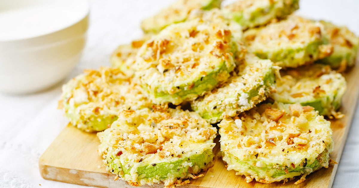 Crispy baked zucchini slices coated in breadcrumbs and cheese arranged on a wooden board.