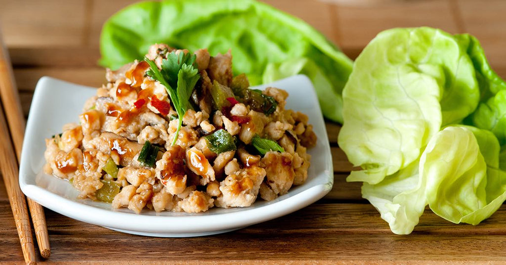Plate of saucy minced chicken with vegetables, served alongside fresh lettuce leaves for wrapping.