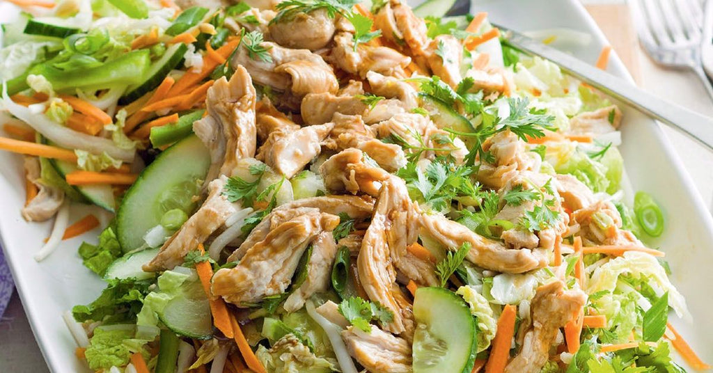 Shredded chicken salad with cucumbers, carrots, cabbage, and fresh herbs on a white plate.