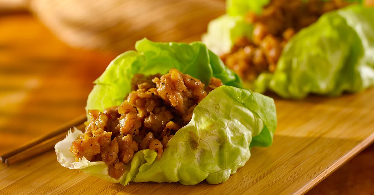 Lettuce cups filled with seasoned ground chicken on a wooden board.