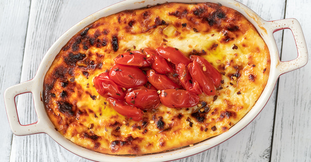Baked cheesy dish with a golden crust, topped with roasted red tomatoes in a white casserole dish.