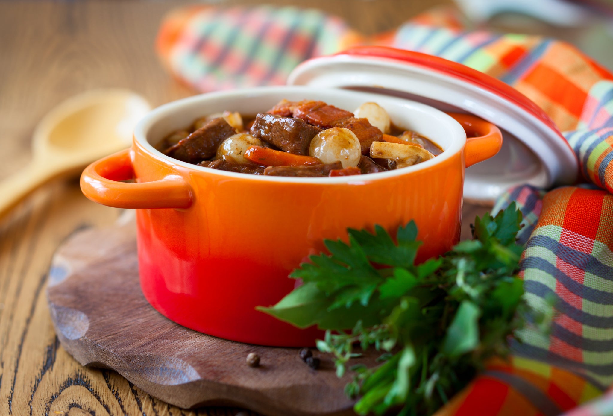Beef stew with vegetables served in an orange pot, garnished with fresh herbs on a wooden board.