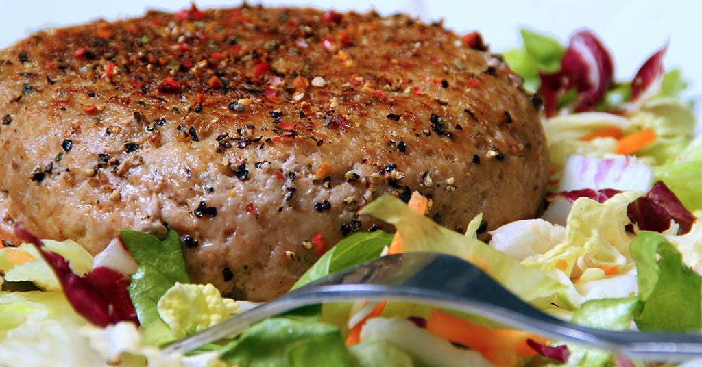 A seasoned, round veggie patty sits atop a colorful bed of fresh salad greens, with a fork resting beside it, highlighting a healthy meal option.
