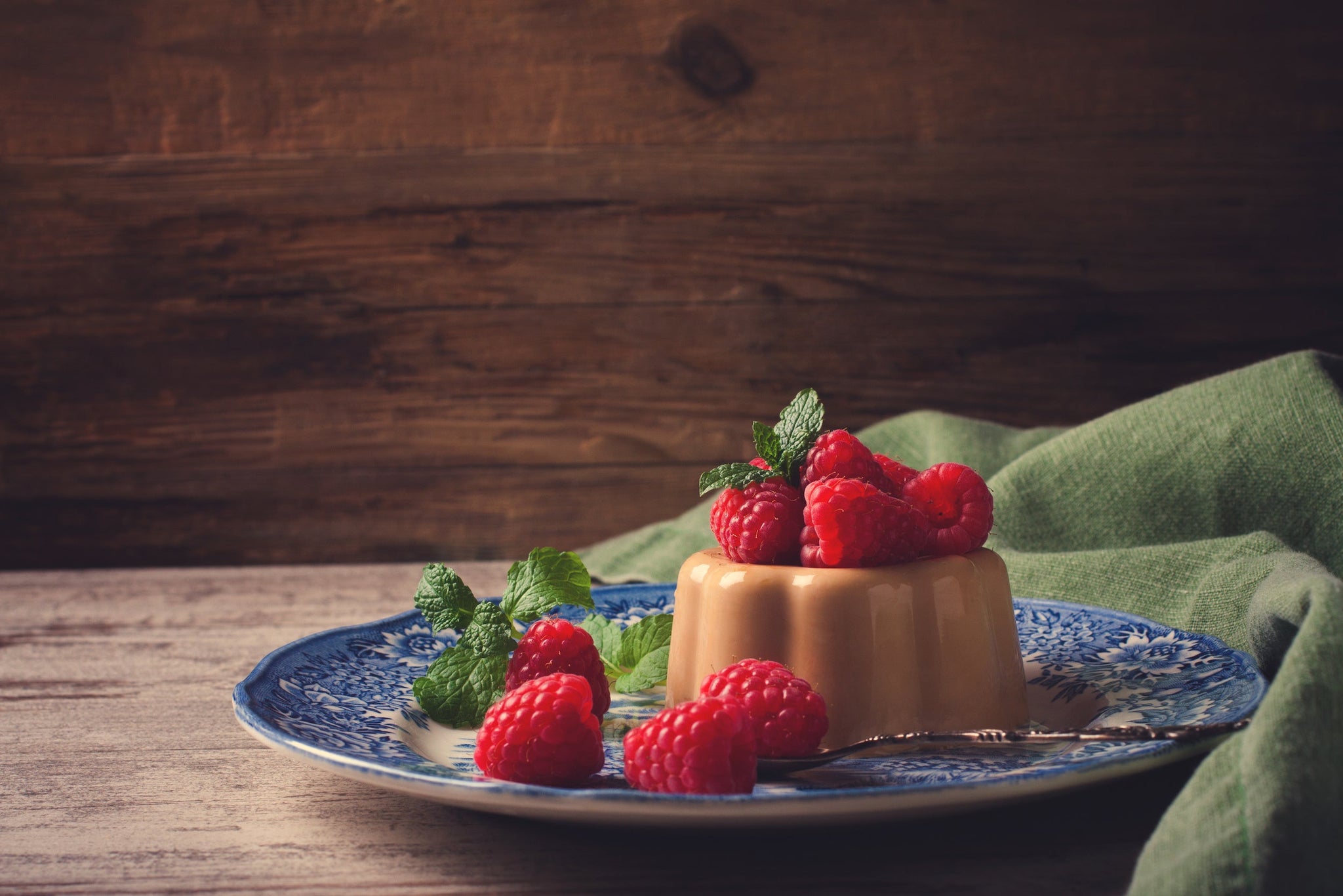 Caramel panna cotta topped with fresh raspberries and mint on a blue plate.