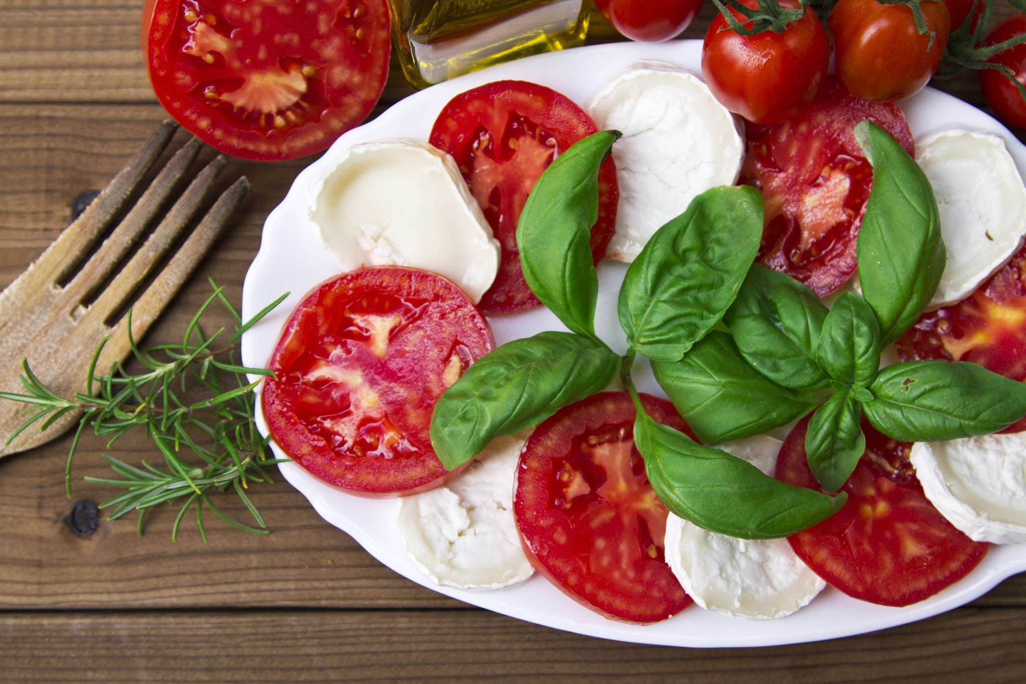 Plate of sliced tomatoes and mozzarella topped with fresh basil leaves on a wooden table.