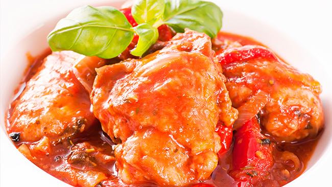 Chicken pieces simmered in a rich tomato and pepper sauce, garnished with fresh basil.