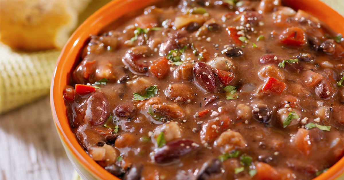 Close-up of a hearty bean and vegetable stew in an orange bowl, topped with herbs.