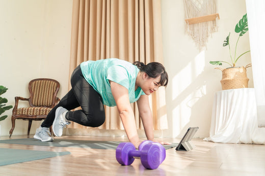 Woman doing a workout at home, following a tablet video, with purple dumbbells on the floor.