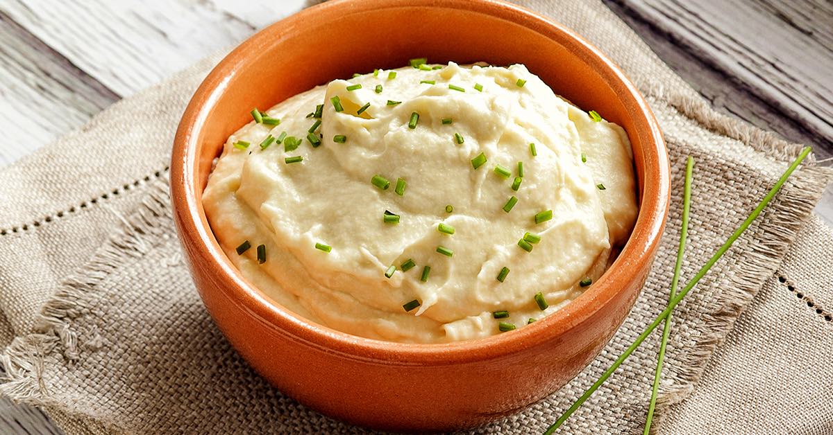 Bowl of creamy mashed potatoes topped with chopped chives on a rustic cloth.