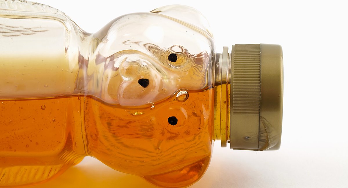 Plastic bear-shaped honey bottle lying on its side with golden honey visible inside.