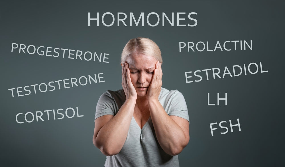 A woman with blonde hair holds her head in distress against a dark background, surrounded by words related to hormones, highlighting the impact of hormonal imbalance on health.