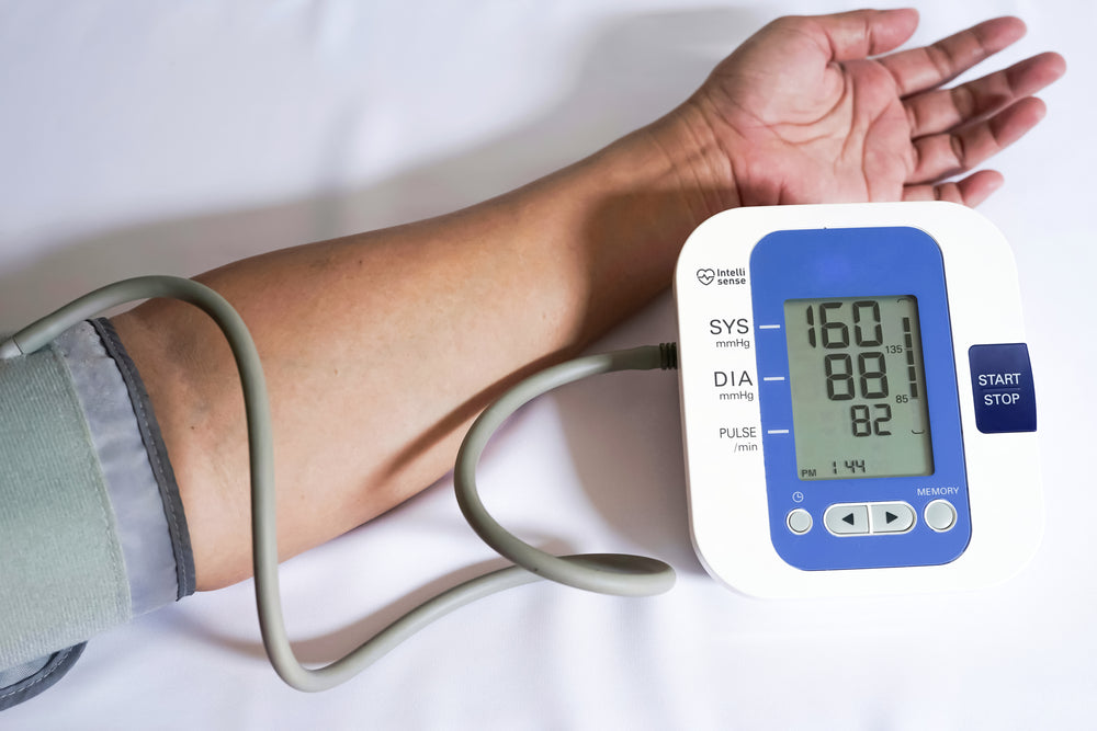 A close-up of a person's arm with a blood pressure cuff attached, displaying a reading of 160/88 on a digital monitor, against a plain white background.