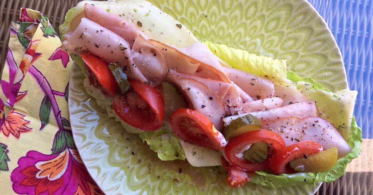 Lettuce wrap filled with sliced deli meat, tomatoes, pickles, and cheese.