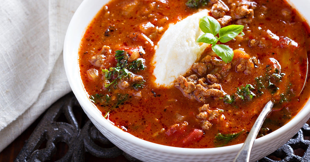 Hearty bowl of tomato-based soup with ground meat, herbs, and a dollop of ricotta, garnished with fresh basil.