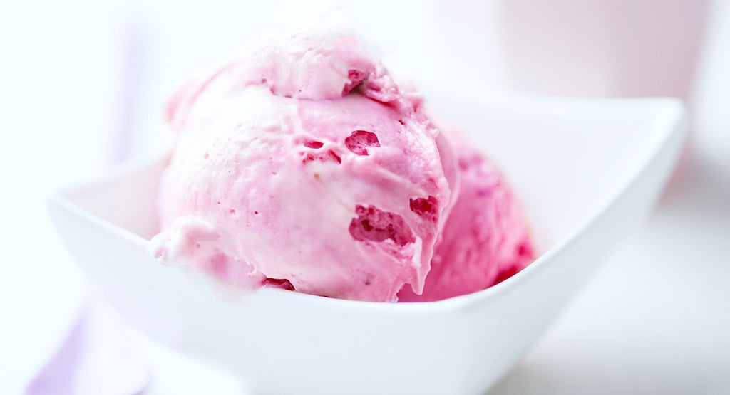 Pink ice cream scoops with berry pieces served in a white bowl.