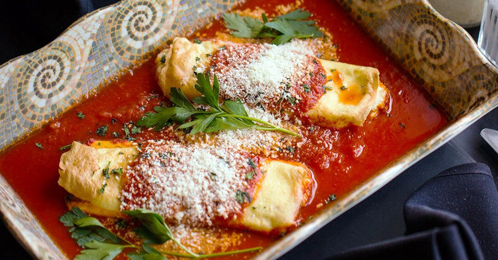 Cheese filled crepes topped with tomato sauce and parmesan, served in a dish with fresh parsley.