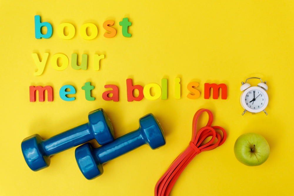 Colorful letters spell "boost your metabolism" on a yellow background, accompanied by blue dumbbells, a red resistance band, a green apple, and a small white alarm clock.