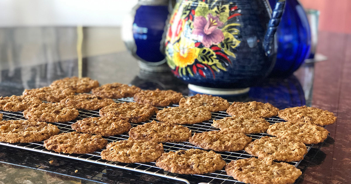 Freshly baked oatmeal cookies cooling on wire racks beside colorful ceramic pottery.