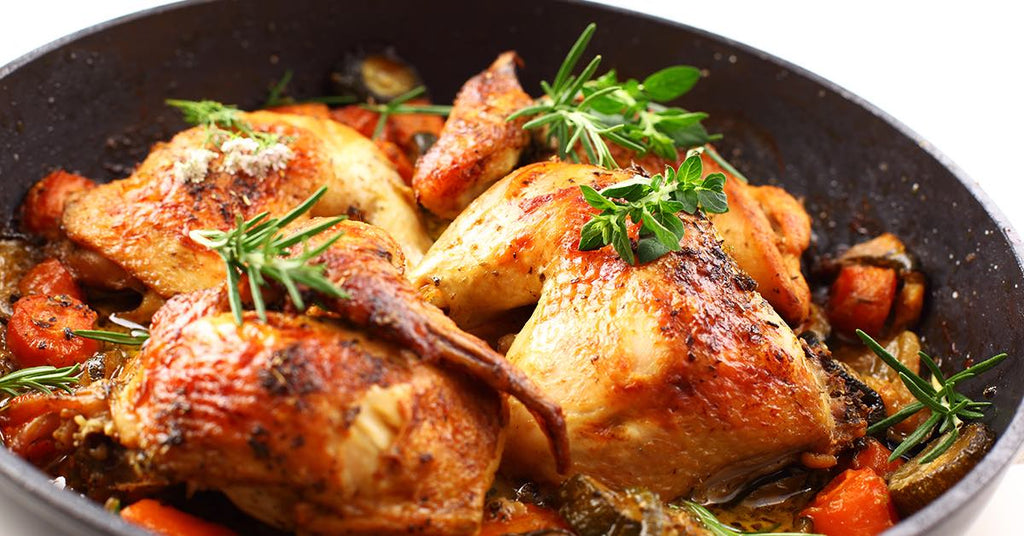 Golden roasted chicken pieces in a pan with herbs, carrots, and vegetables.