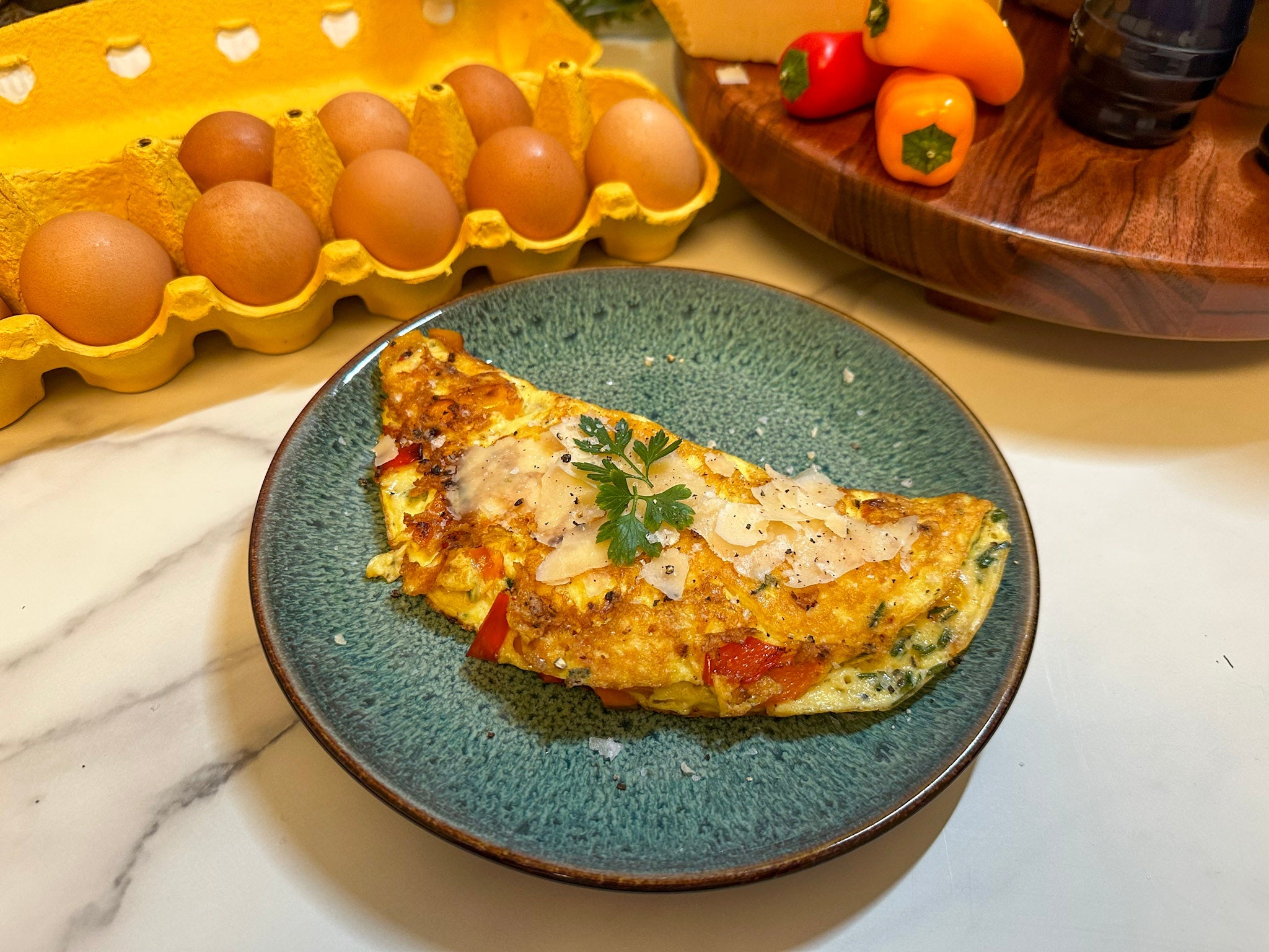 Cheese-topped vegetable omelet on a green plate with eggs and peppers in the background.
