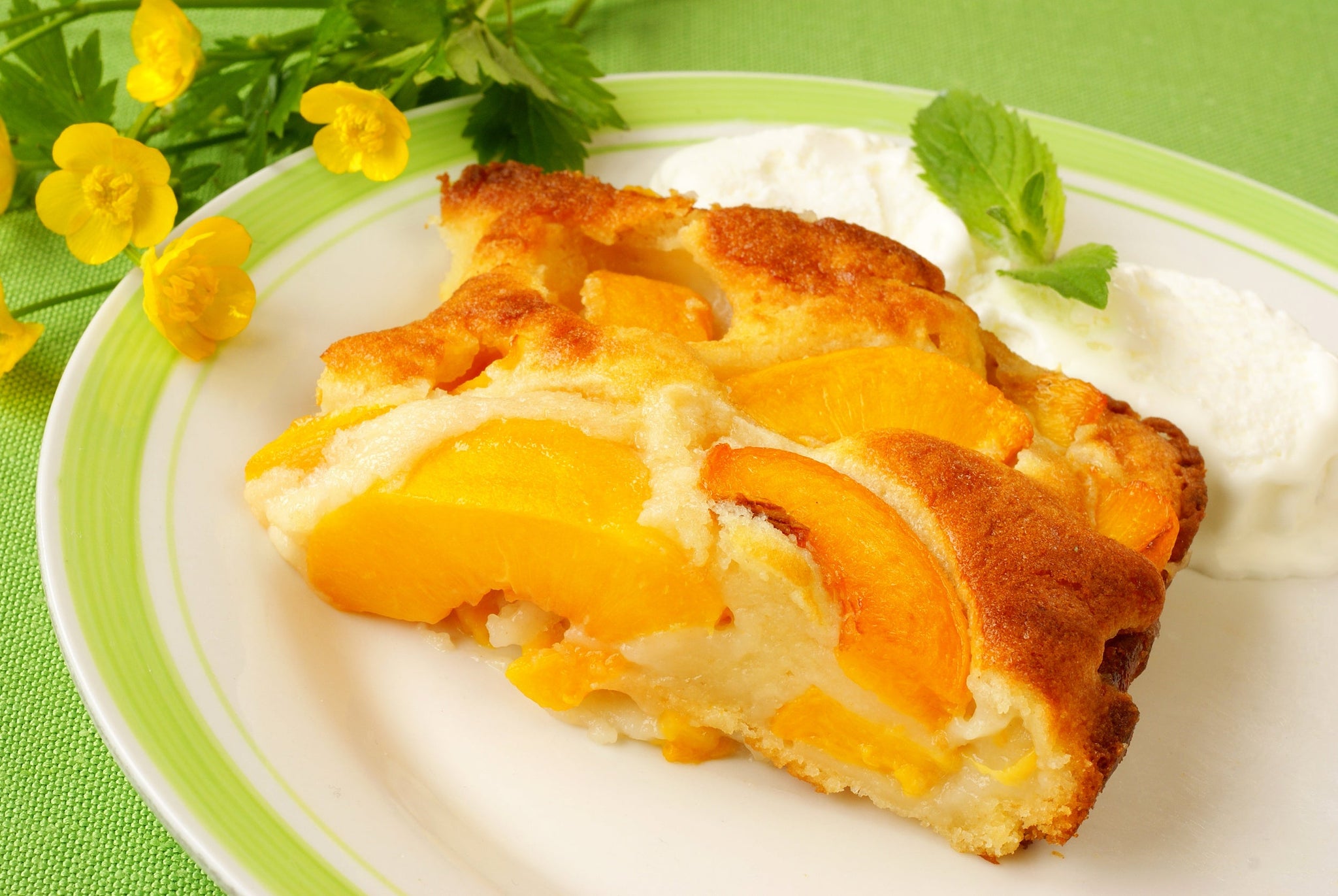 Slice of peach cobbler with golden crust served on a plate with whipped cream and mint.
