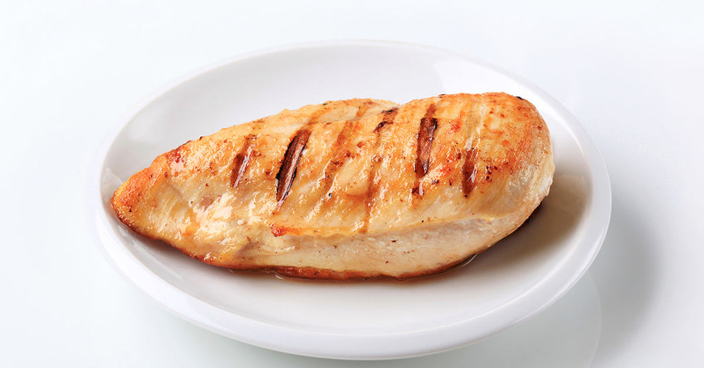 Grilled chicken breast with sear marks served on a white plate.