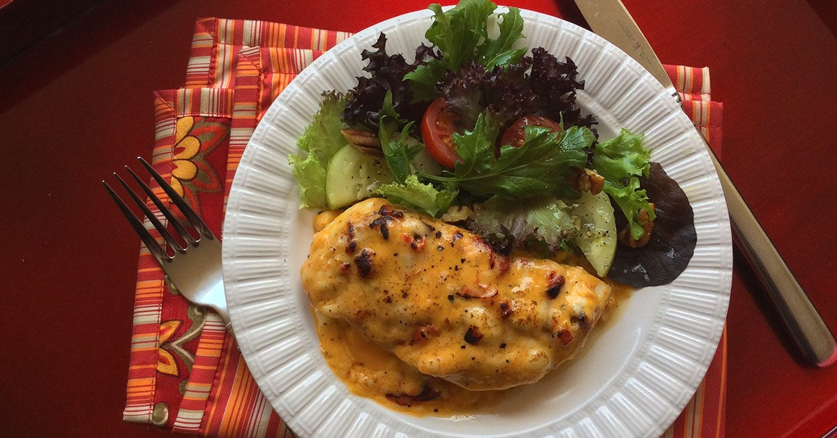 Cheesy baked chicken served with a fresh salad of mixed greens, cucumbers, and tomatoes on a white plate.